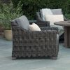 Outdoor wicker club chairs with gray cushions and accent pillows on a stone patio.