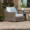Woven wicker club chair with white and blue cushions beside a pool and flowers.