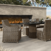 Outdoor wicker dining arm chairs with cushions around a rectangular table by a fireplace.