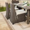 Outdoor wicker dining side chairs with cushions arranged around a wooden table beside a lake.