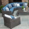 Outdoor wicker sectional with blue cushions and accent pillows arranged around a coffee table on stone patio.