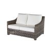 Woven wicker loveseat with white cushions in hickory finish.