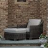 Outdoor wicker chair paired with matching ottoman on a stone patio.
