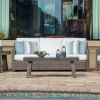 Outdoor wicker sofa with white cushions and striped pillows beside a pool.