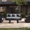 Outdoor wicker sofa with gray cushions and black pillows on a wooden deck.