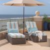 Pair of Laurent wicker cushion chaise lounges in Chestnut finish with striped cushions and umbrella on a balcony.