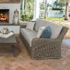 Laurent wicker cushion sofa with neutral cushions styled by an outdoor fireplace and rustic coffee table.