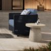 Outdoor Pompano 20″ Round Patio Side Table with beige shell base beside navy wicker lounge chair