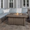 Trevi Fire Pit Table in Hickory shown on a patio with wicker sectional seating.