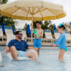 Adult relaxing in a white Forma in-pool chair with children playing on a shallow pool shelf