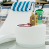 White Forma in-pool side table holding sunscreen, goggles, and a drink beside an in-pool chaise lounge