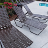 Sundance stackable aluminum cross-weave chaise lounges with dark frames and gray woven vinyl straps arranged around a commercial pool